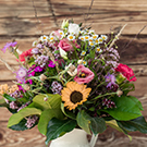 Ein bunter Blumenstrauß in einer Vase, bestehend aus verschiedenen Blumen wie Sonnenblumen, Rosen und Wildblumen, umgeben von grünem Laub. Der Strauß strahlt Frische und Farbenvielfalt aus und hat einen rustikalen Hintergrund aus Holz.