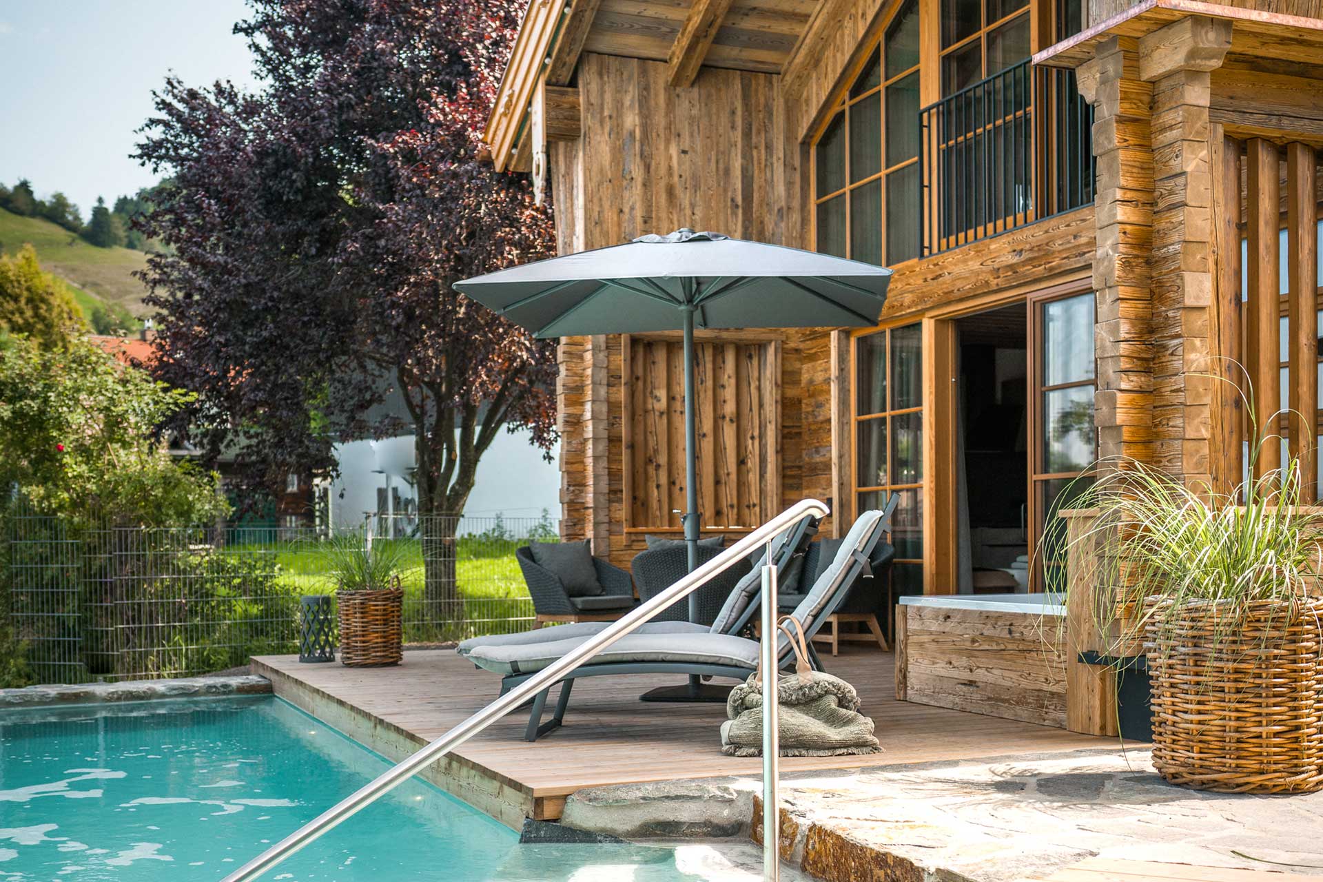 Aussenaufnahme mit Schirm, Terrrasse, Naturbadesee, Lounge und Whirlpool des Premium Plus Chalets