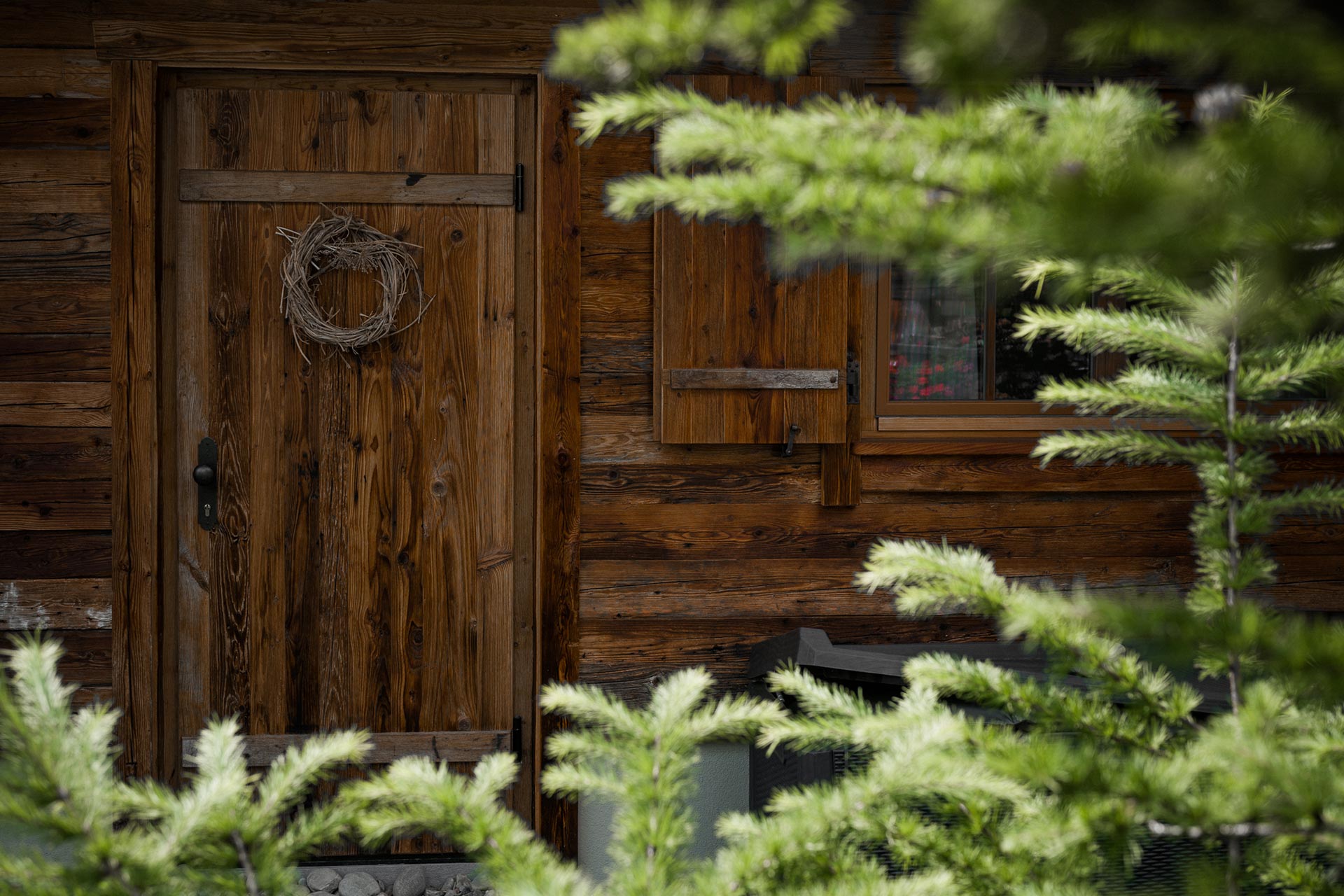 Türe eines Chalet, mit Pflanzen im Vordergrund und Schellen hängend oberhalb von Türe