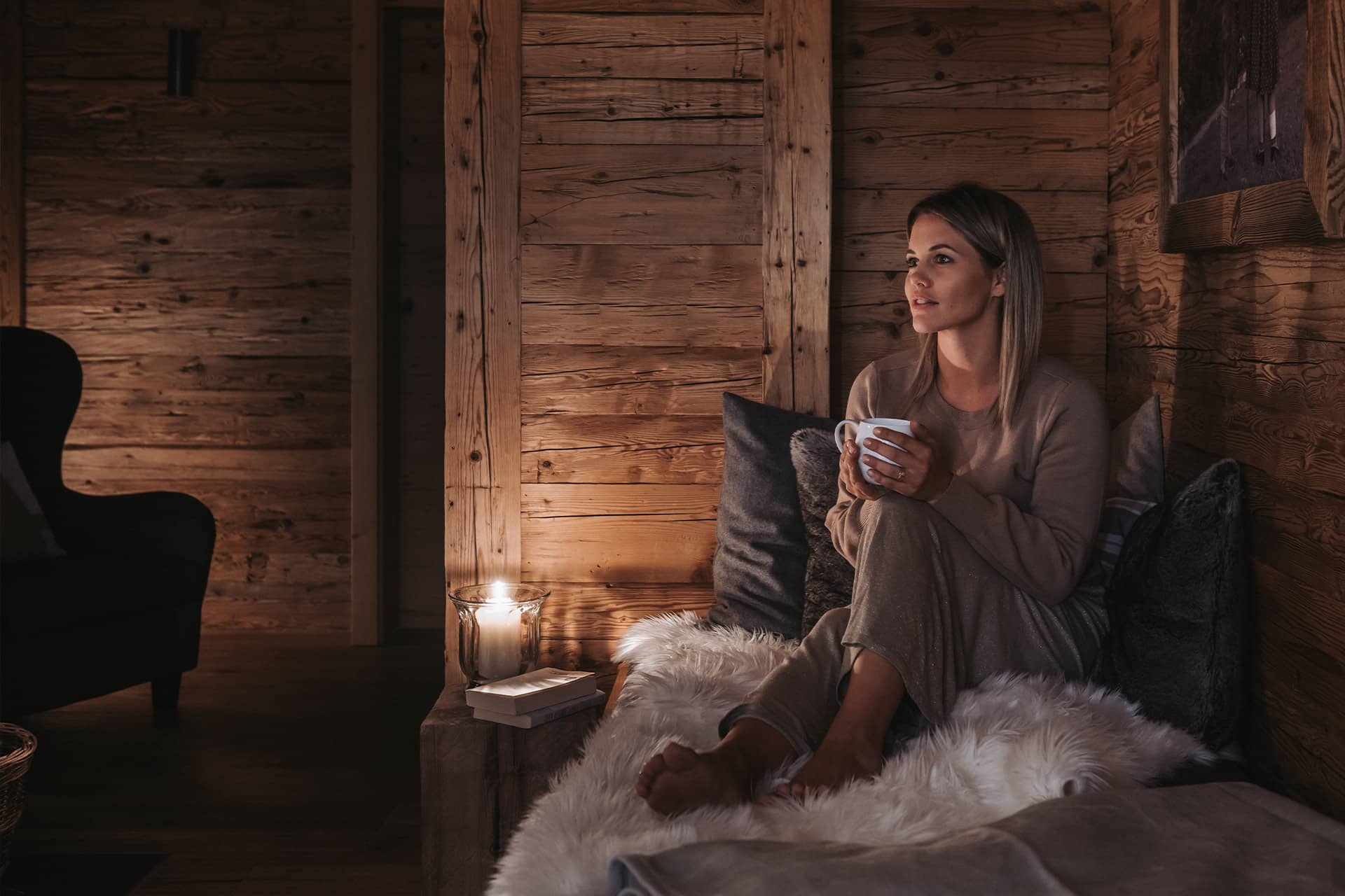 Eine Frau genießt die Abendstimmung in Ihrem Chalet und sitzt gemütlich mit einer Tasse Tee im Kerzenschein
