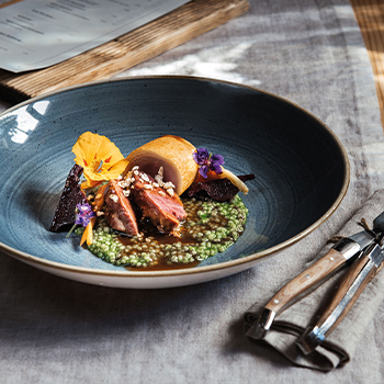 Ein kunstvoll angerichteter Teller mit zartem Fleisch, begleitet von grüner Petersiliencreme, dekoriert mit essbaren Blumen und Kräutern. Die harmonische Farbkomposition verleiht dem Gericht eine ansprechende Ästhetik.